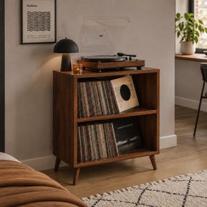May include: A dark wood record storage cabinet with two open shelves filled with vinyl records. The top surface holds a black turntable and a small black mushroom-shaped lamp. The cabinet features four tapered legs and a rectangular frame.