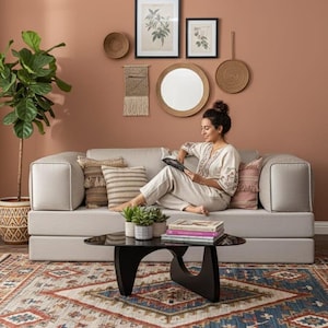 Puede incluir: Un sal&oacute;n con un sof&aacute; gris claro con cojines decorativos, una mesa de centro negra y una alfombra estampada. La pared est&aacute; adornada con estampas bot&aacute;nicas enmarcadas y objetos tejidos. Una planta en maceta a&ntilde;ade un toque de vegetaci&oacute;n.