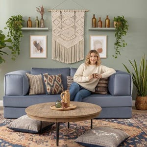 Puede incluir: Un sal&oacute;n acogedor con un sof&aacute; azul, cojines decorativos, una mesa de centro redonda de madera y una alfombra estampada. La habitaci&oacute;n est&aacute; decorada con plantas, obras de arte y un tapiz de macram&eacute;, creando un ambiente c&aacute;lido.