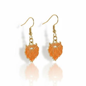 May include: A pair of gold-colored earrings, each featuring a stylized orange beard design with a gold outline. The earrings hang from gold-colored fish hook ear wires.