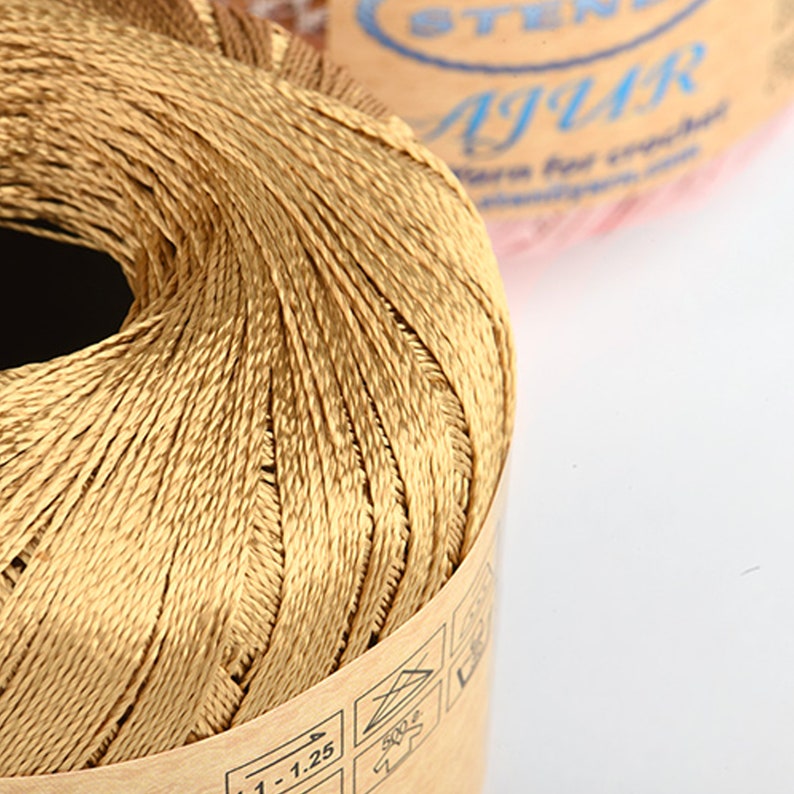 May include: A spool of gold-colored thread with a brown paper label that says "1-1.25" and has a washing instructions icon. The label also has the word "Jaguar" on it.