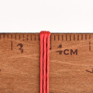 May include: Close-up of a red string measured against a wooden ruler marked in centimeters. The string is about 3 centimeters long.