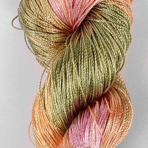 May include: A skein of peach, pink, and green silk thread. The thread is wound into a ball shape and is labeled "TENALI".