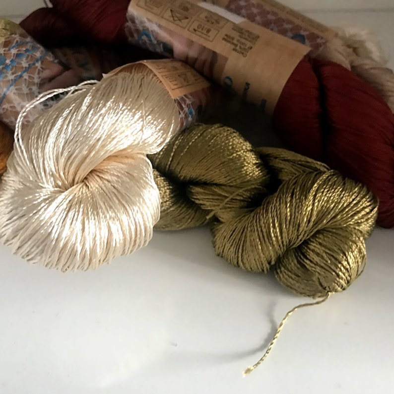 May include: Three spools of embroidery floss in different colors: a cream color, a dark green, and a burgundy red.
