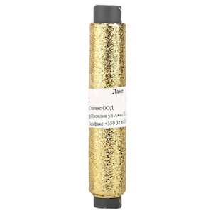 Peut inclure: Bobine de fil métallique doré, étiquetée "Lame". Le fil est enroulé autour d'une âme cylindrique avec des capuchons gris foncé aux extrémités. L'étiquette contient également du texte en langue étrangère. Idéal pour la broderie.