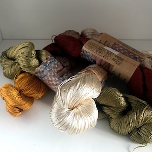 May include: Assortment of spools of colorful silk thread, including gold, green, cream, and red. The thread is wound around cardboard spools with labels that include care instructions.