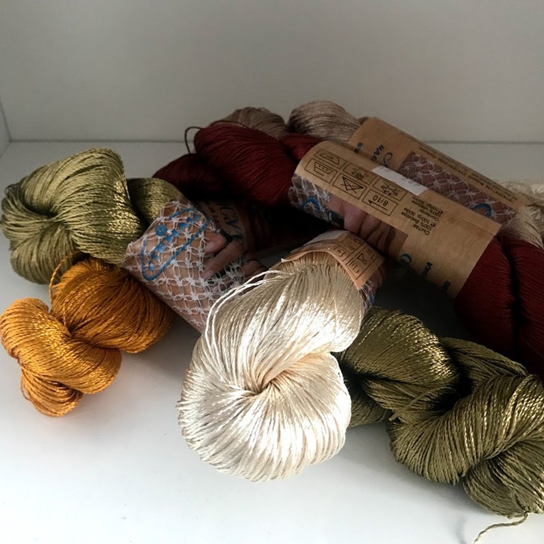 May include: Assortment of spools of colorful silk thread, including gold, green, cream, and red. The thread is wound around cardboard spools with labels that include care instructions.