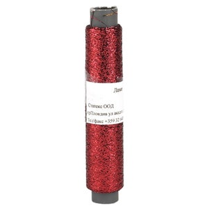 Op de afbeelding: Een spoel rood glittergaren met een wit etiket. De draad is gewikkeld rond een grijze plastic kern. Het etiket heeft tekst in een vreemde taal.