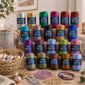 Puede incluir: Una colección de veinte bobinas de hilo Stenli Brocat en varios colores metálicos, cada una con una etiqueta azul. El hilo está dispuesto en filas, acompañado de artículos decorativos que incluyen una cesta de ganchillo dorada, adornos y una alfombrilla circular.