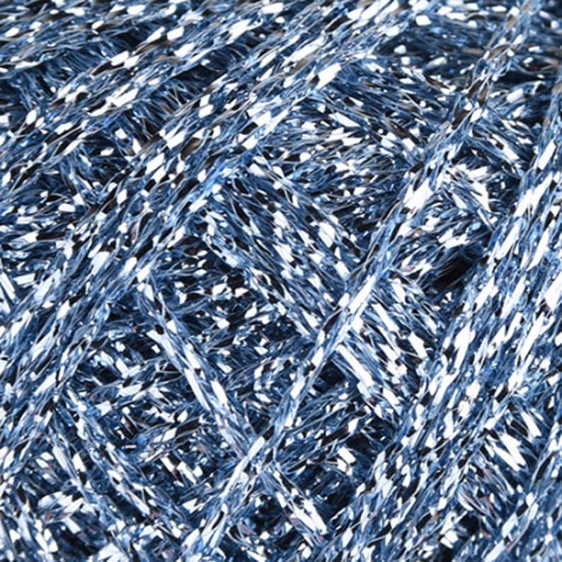 May include: A dense, tightly wound ball of metallic light blue yarn. The strands feature a highly reflective, shimmering finish that creates a bright, multi-faceted appearance with intersecting lines of silver and cool blue tones throughout.