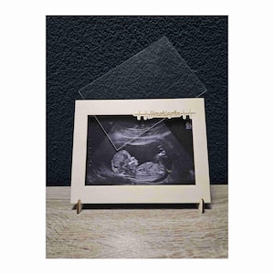 Könnte beinhalten: Ein Holzrahmen mit einem Ultraschallbild eines Babys. Der Rahmen hat den Schriftzug "Herzklopfen" und ein Herzschlagsymbol. Eine transparente Acrylplatte liegt oben auf dem Rahmen.