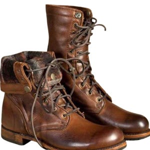 May include: A pair of brown leather lace-up boots featuring a mid-calf height, a rounded toe, and a fold-over cuff lined with a dark patterned fabric. The boots include metal eyelets, brown laces, and a stacked heel with a visible rubber sole.