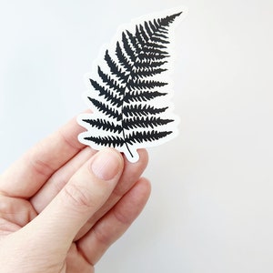 Puede incluir: Una pegatina de hoja de helecho negra sobre un fondo blanco.