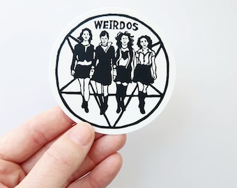 Peut inclure: Un autocollant noir et blanc avec un pentagramme et quatre figures de femmes dans un cercle. Le texte "WEIRDOS" est en haut du cercle.