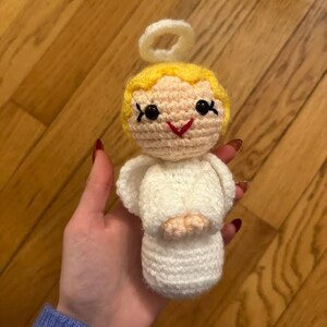 May include: A handmade crochet angel doll with a white dress, wings, and halo. The doll has yellow hair, black eyes, and a red smile. The doll is approximately 4 inches tall.