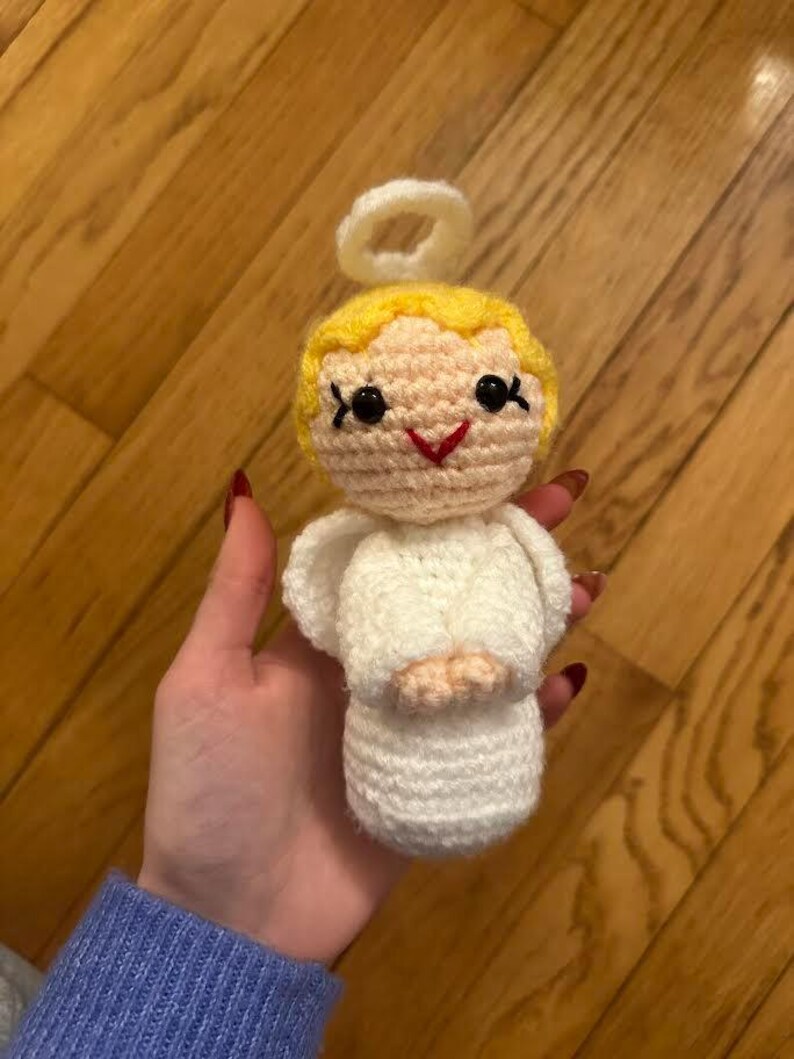May include: A handmade crochet angel doll with a white dress, wings, and halo. The doll has yellow hair, black eyes, and a red smile. The doll is approximately 4 inches tall.