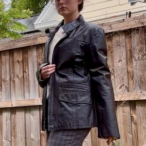 May include: A white ceramic mug with a black handle and the text "But First, Coffee" in a bold, black font. The mug is set against a blurred background, suggesting a cozy setting.