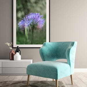 May include: A framed print of a blurred purple flower. A teal armchair with wooden legs is placed on a patterned rug. Decorative vases are on a white cabinet, creating a modern interior design.