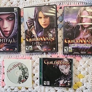 May include: A collection of Guild Wars PC game boxes and a CD. The boxes feature female characters with fantasy themes. Titles include Nightfall, Factions, and Eye of the North. The CD has a Guild Wars logo.