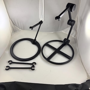 Puede incluir: Soportes de teléfono negros ajustables con bases circulares y en forma de cruz. Los soportes tienen brazos articulados y pequeños soportes curvos. También se incluyen dos pares de accesorios negros en forma de barra.