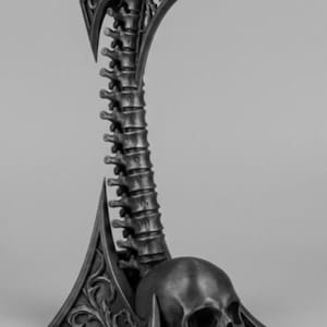 May include: A dark grey headphone stand with a gothic design. It features a spine-shaped central column, a skull at the base, and decorative, pointed elements. The design evokes a medieval aesthetic.