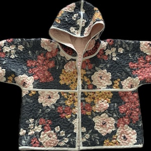 May include: A quilted jacket with a floral pattern in shades of pink, yellow, and white on a dark blue background. The jacket has a hood and is lined with a light pink fabric. The edges are trimmed with white.