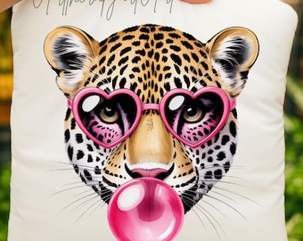 May include: White square pillow featuring a leopard face with pink heart-shaped sunglasses and a pink bubble gum bubble. The leopard has a spotted coat and is centered on the pillow. The text "A therapy art Art" is written in cursive on the pillow.