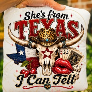 May include: White cushion featuring a Texas-themed design. The design includes a skull with horns, a leopard print cowboy hat, the Texas flag, playing cards, cherries, dice, and the text "She's from TEXAS I Can Tell."