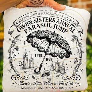 May include: A white square throw pillow featuring a black graphic print of an ornate parasol, five lit candles, and a skull. The text reads: ROOFTOP JUMP & MARGARITAS AT MIDNIGHT, OWEN SISTERS ANNUAL PARASOL JUMP, ESTD 1998, There's a Little Witch in All of Us, MARIA'S ISLAND, MASSACHUSETTS.