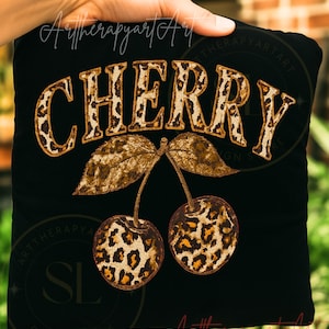 Op de afbeelding: Zwart vierkant kussen met het woord "CHERRY" in een vintage luipaardprint lettertype. Daaronder twee kersen met luipaardprint en bruine bladeren. Het ontwerp wordt door een hand vastgehouden.
