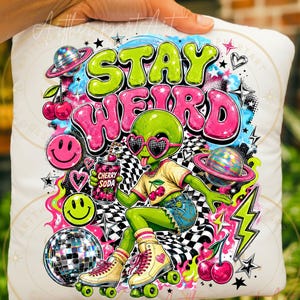 May include: A white square pillow featuring a colorful graphic of a green alien wearing heart-shaped sunglasses and roller skates. The design includes the text STAY WEIRD, a cherry soda can, a disco ball, planets, cherries, and smiley faces.