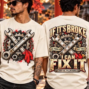 May include: An off-white t-shirt featuring a graphic of crossed wrenches, a gear, and a red cloth. The back design includes the text: IF IT'S BROKE NO PROBLEM JUST TOOLS I CAN FIX IT TRUST ME, I'M A MECHANIC in a distressed, bold font.