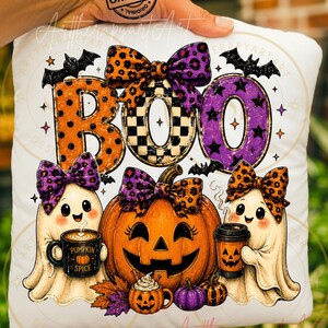 May include: A white square cushion featuring the text BOO in large letters with orange polka dot, black and white checkerboard, and purple star patterns. Two ghosts with colourful bows hold pumpkin spice coffee cups near a large jack-o'-lantern.