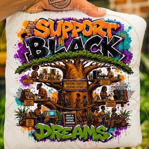 May include: A white throw pillow featuring a vibrant graphic of a large baobab tree with various scenes of people working in branches. The text reads SUPPORT BLACK DREAMS, BUILDING LEGACIES CREATING FUTURES, INVEST IN COMMUNITY EMPOWER GENERATIONS, ART, BOOKS, COFFEE, FASHION, and TECH.