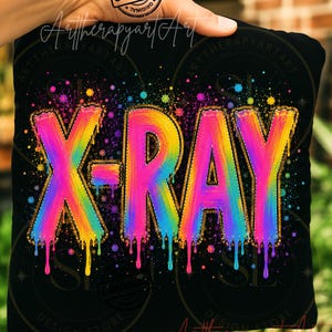 May include: A black fabric item featuring the text X-RAY in a vibrant, multi-colored rainbow gradient with a paint-drip effect. The letters are outlined in a gold-toned stitch pattern, surrounded by colorful paint splatters on a dark background.
