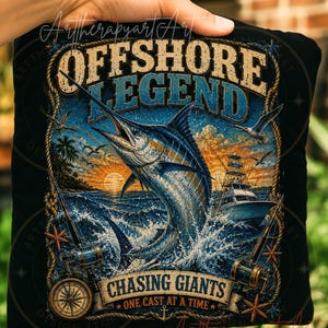 May include: A black t-shirt featuring a graphic print of a marlin jumping out of the ocean at sunset. The text reads OFFSHORE LEGEND, CHASING GIANTS, and ONE CAST AT A TIME. The design includes a fishing boat, two fishing rods, a compass, and starfish.