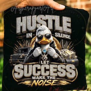 May include: Black pillow with a graphic of a duck wearing sunglasses and a hoodie, with the words "HUSTLE IN SILENCE LET SUCCESS MAKE THE NOISE" in a diamond-like font. The duck is wearing a diamond necklace and a watch. A black car, stacks of money, and a briefcase are also in the image.