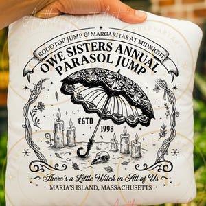 May include: A white square cushion featuring a black and white graphic. The design includes a parasol, candles, and text that reads "Owe Sisters Annual Parasol Jump" and "There's a Little Witch in All of Us."