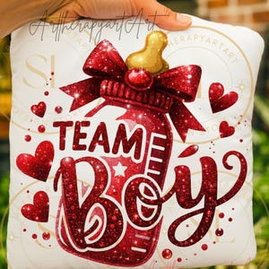 May include: A white pillow with a red glitter design that says "TEAM BOY". The design includes a baby bottle with a red bow, a gold nipple, and red hearts. The pillow is held by a hand.
