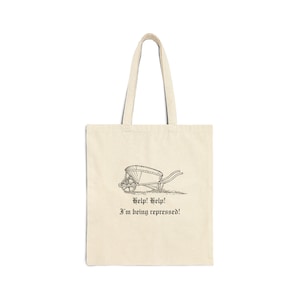May include: Cream-colored tote bag with a black line drawing of a wheelbarrow. The wheelbarrow has a canopy and is on a grassy surface. Below the image are the words "Help! Help! I'm being repressed!"