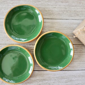 Op de afbeelding: Drie kleine groene keramische schalen met gouden randen. De schalen zijn gerangschikt op een licht houten oppervlak.