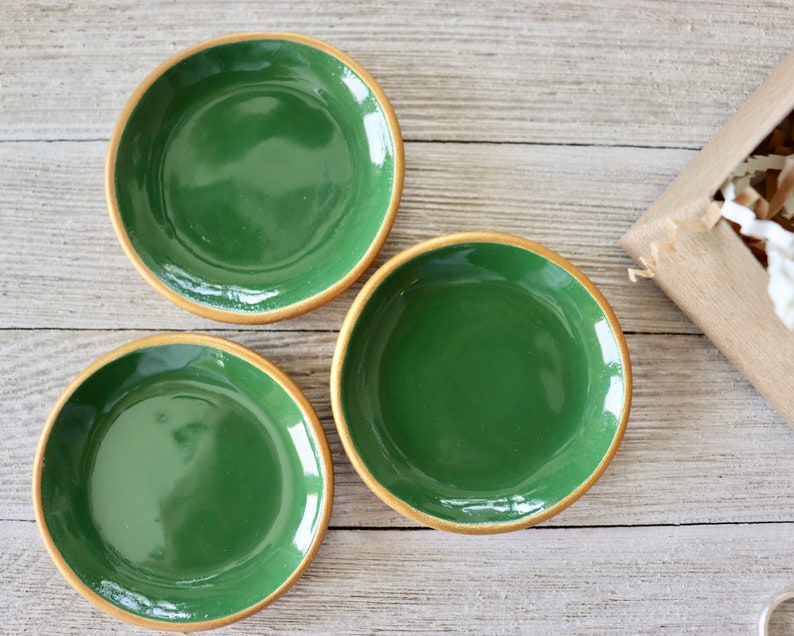 Op de afbeelding: Drie kleine groene keramische schalen met gouden randen. De schalen zijn gerangschikt op een licht houten oppervlak.