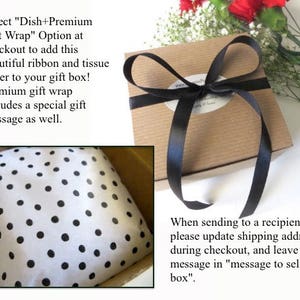 Op de afbeelding: Een bruine cadeaudoos met een zwart lint eromheen gebonden. De doos is verpakt in wit tissuepapier met zwarte stippen. De tekst "Select "Dish+Premium Gift Wrap" Option at checkout to add this beautiful ribbon and tissue paper to your gift box! Premium gift wrap includes a special gift message as well." is zichtbaar in de afbeelding.
