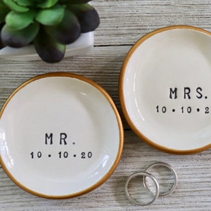 May include: Two white ceramic ring dishes with gold rims. The dishes are labelled "MR. 10.10.20" and "MRS. 10.10.20".