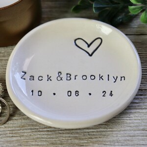 Op de afbeelding: Witte keramische ringenschotel met een handgetekend hart en de tekst "Zack & Brooklyn 10.06.24".