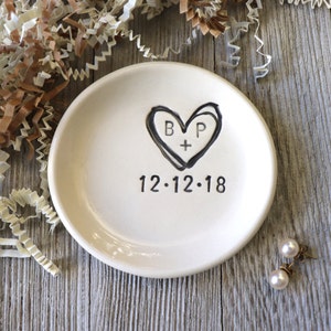 Puede incluir: Plato de anillo de cerámica blanca con un diseño de corazón negro y las iniciales "B + P" dentro del corazón. La fecha "12.12.18" está escrita debajo del corazón.