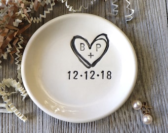 May include: White ceramic ring dish with a black heart design and the initials "B + P" inside the heart. The date "12.12.18" is written below the heart.
