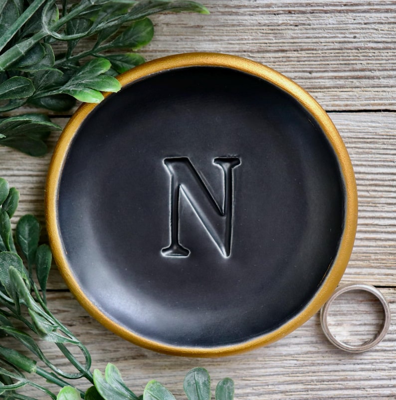 May include: A black ring dish with a gold rim and the letter "N" embossed in the center.
