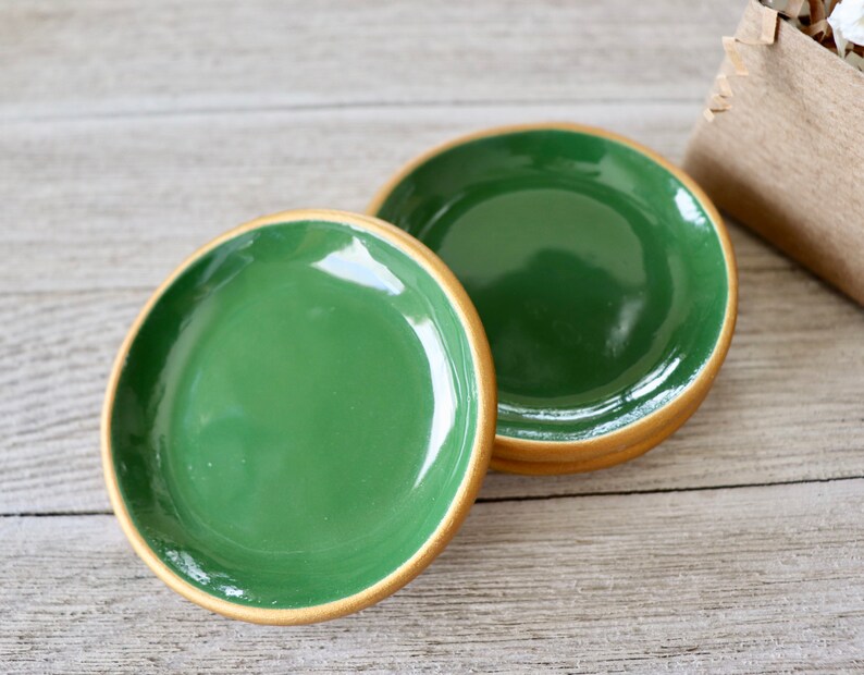 Op de afbeelding: Drie groene keramische sierborden met een gouden rand. De borden zijn op elkaar gestapeld.