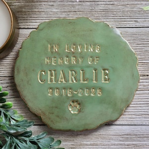 May include: A green ceramic memorial plaque with the text "In loving memory of Charlie 2016-2025" and a paw print.
